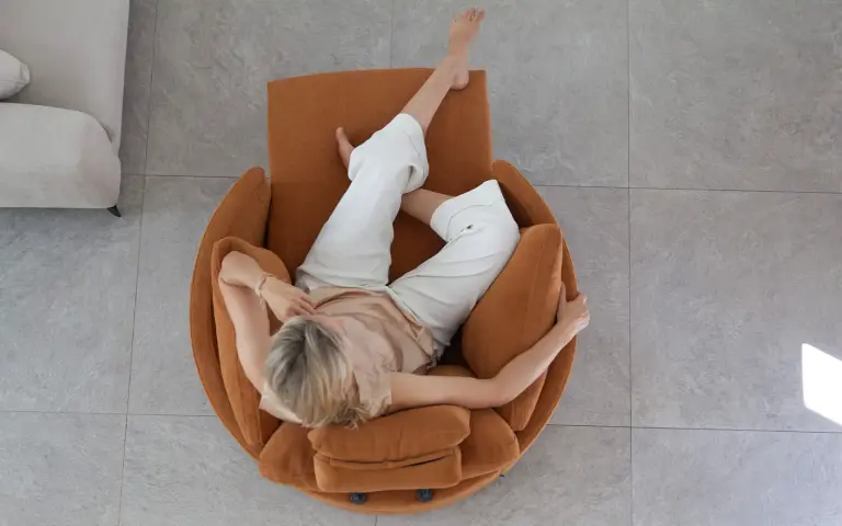 Sillón relax Moonrise de Fama Sofás tapizado en tela color ocre oscuro, con cabecero ajustable y diseño envolvente de líneas redondeadas